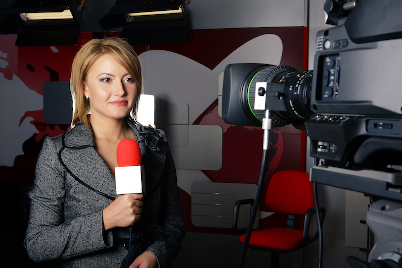 Television news reporter in live transmission smiling in front of the video camera in studio