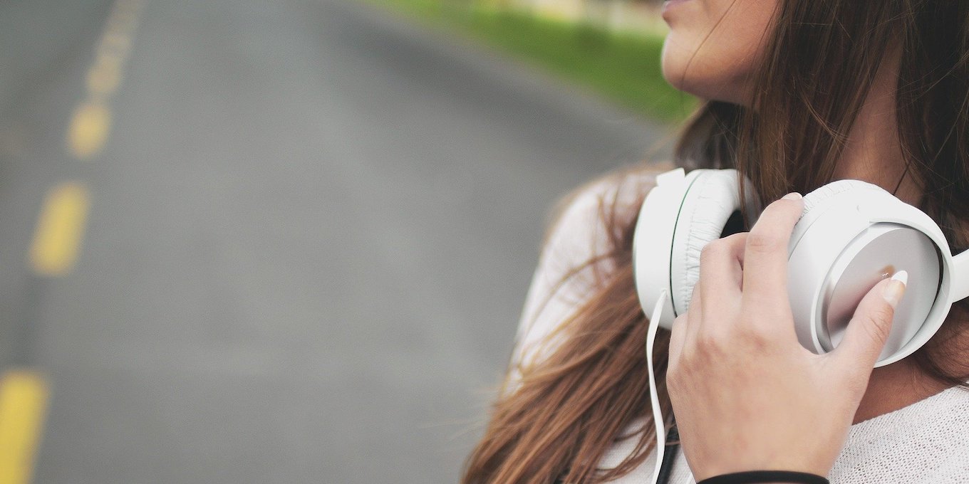 「メンタルを強くする音楽とは」という記事中のイメージ画像です。路上で女性が白いヘヘッドホンを首にかけて音楽の余韻にひたっています。
