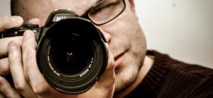 おすすめの宣材写真でオーディションの合格を勝ち取ろう、という記事中のイメージ画像です。カメラマンがファインダーをのぞきカメラのレンズをこちらへ向けています。