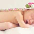 新生児モデルにはどうすればなれるの？という記事中のイメージ画像です。かわいいニットのキャップをかぶった新生児がシーツの上ですやすや眠いっています。