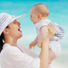 赤ちゃんの生後1ヶ月の成長について書かれた記事中のイメージ画像です。海辺で赤ちゃんを抱きあげるママの笑顔が印象的です。